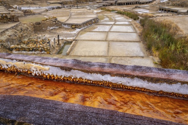 Salt crusts and mineral deposits visible on wooden channels carrying saline water to evaporation ponds, showcasing traditional salt production in the historic anana salt valley