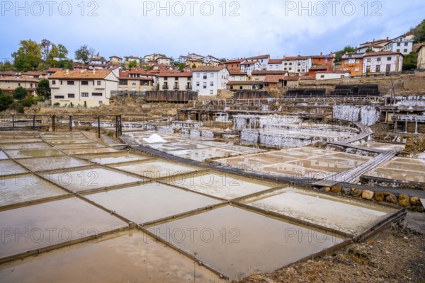 Ancient salt pans and evaporation terraces, with traditional village buildings in the background, showing the historical salt production process at anana