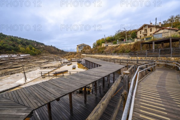Anana salt valley showcasing traditional salt evaporation ponds, wooden structures, and a historical process of salt production under an overcast sky, with buildings on a hillside