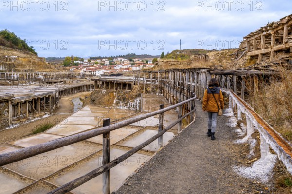 Woman walking along a path next to the historic terraced salt evaporation ponds of the salt valley, an old, traditional industry in the basque country