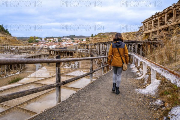 Woman exploring the ancient salt flats of anana, finding herself immersed in the historical landscape with traditional salt pans and a captivating village in the background