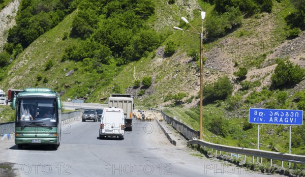 A road with vehicles in a mountainous landscape, green hills and a sign with a river name, bridge over the Aragvi River, Kvemo Mleta, Mtskheta-Mtianeti region, Georgian Military Highway, High Caucasus, Georgia