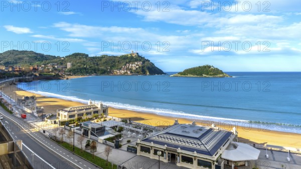 La concha bay beach with golden sand, santa clara island and mount igueldo rising above san sebastians hillside cityscape, sunny seaside panorama ideal for travel