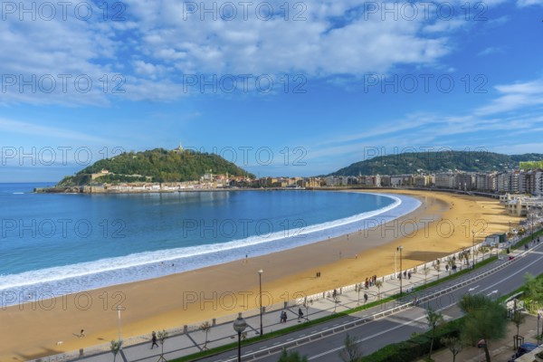 La concha beach curving along the bay of san sebastian city, with people walking on the sand and promenade, overlooking monte igueldo and the urban coastline under a bright blue sky