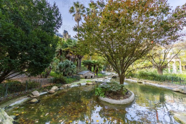 Gipuzkoa square showcasing a tranquil pond and green trees with hints of autumn foliage, reflecting the surrounding architecture and vegetation in a basque country urban park setting