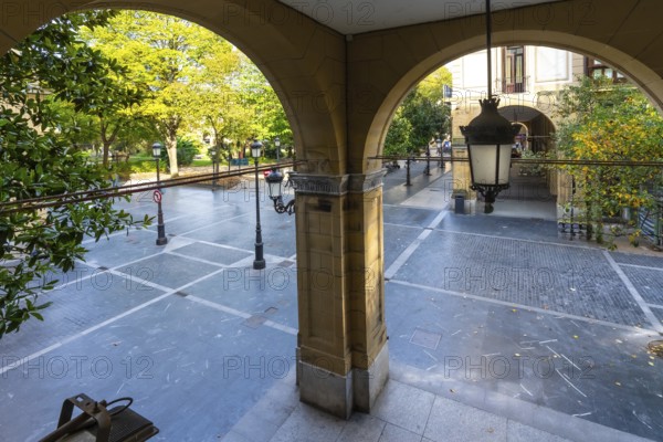 Arched arcade entrance providing a view through to gipuzkoa square park in san sebastian, featuring autumn trees, traditional street lamps, and historical architecture