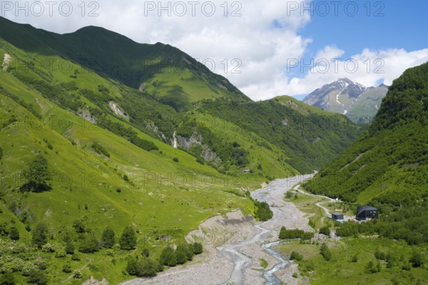 Wide mountainous landscape with river surrounded by lush greenery under a cloudy sky, White Aragvi River, Mtskheta-Mtianeti region, Georgian Military Highway, High Caucasus, Georgia