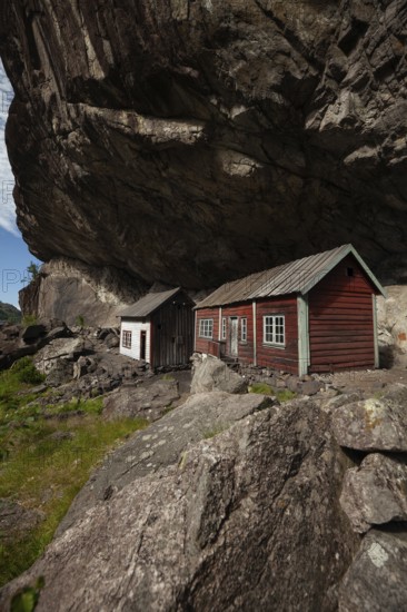 Historical wooden houses sheltered under a massive rock overhang. Summer, Helleren (Helleren), Rogaland, Norway