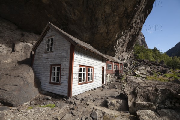 Historical wooden houses sheltered under a massive rock overhang. Summer, Helleren (Helleren), Rogaland, Norway