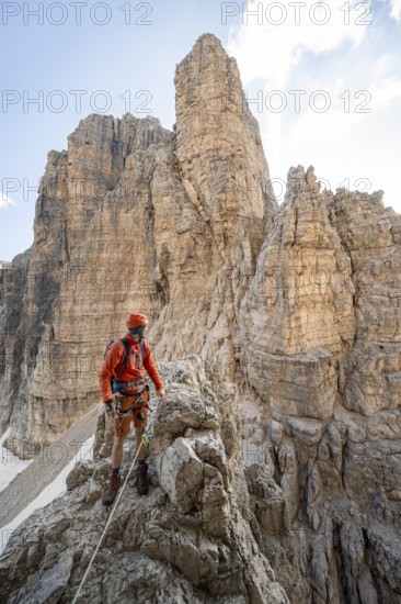 Mountaineer climbs on an exposed rock in the secured Via Ferrata Bocciere Centrale via ferrata, mountain landscape with spectacular rock towers in the back, Brenta-Adamello Nature Park, Trentino, Italy
