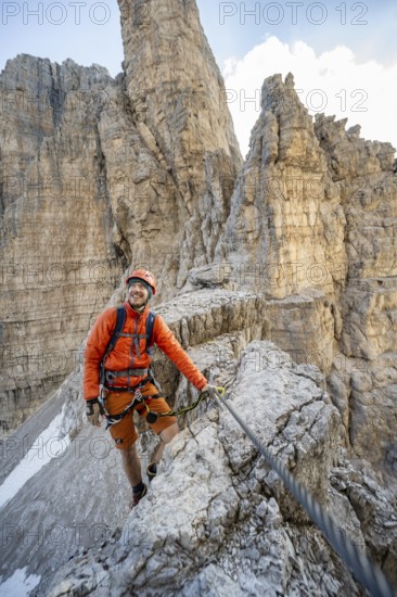 Mountaineer climbs on an exposed rock in the secured via ferrata Bocciere Centrale, Brenta Mountains, Parco Naturale Brenta-Adamello, Trentino, Italy