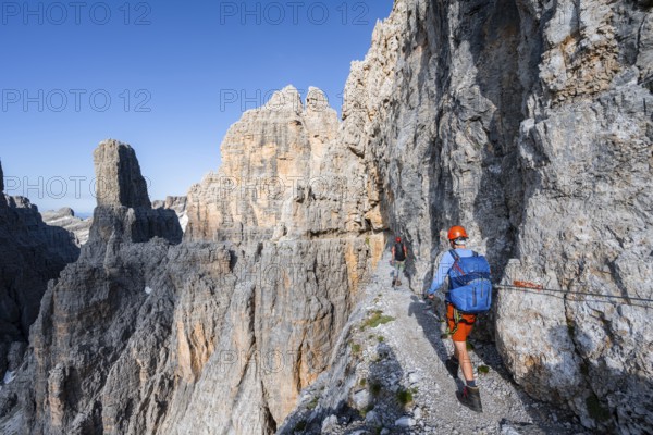 Two mountaineers on an exposed rock band in the secured Via Ferrata Bocciere Centrale via ferrata, spectacular mountain landscape with steep rocky peaks, Brenta Mountains, Parco Naturale Brenta-Adamello, Trentino, Italy