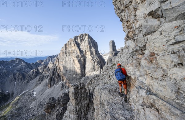 Mountaineer climbs an exposed rock band in the secured Via Ferrata Bocciere Centrale via ferrata, spectacular mountain landscape with steep rocky peaks, Brenta Mountains, Parco Naturale Brenta-Adamello, Trentino, Italy