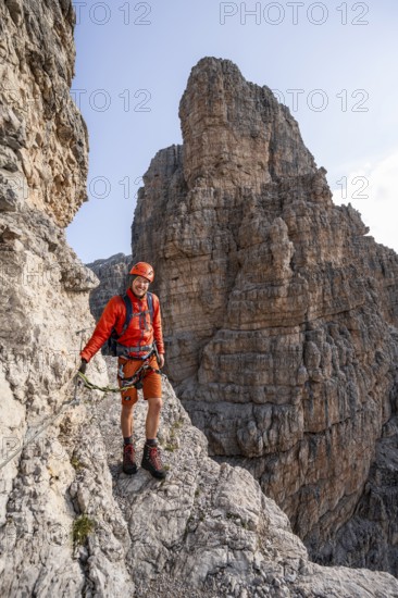 Mountaineer climbs an exposed rock band in the secured Via Ferrata Bocciere Centrale via ferrata, spectacular mountain landscape with steep rock faces, Brenta Mountains, Parco Naturale Brenta-Adamello, Trentino, Italy