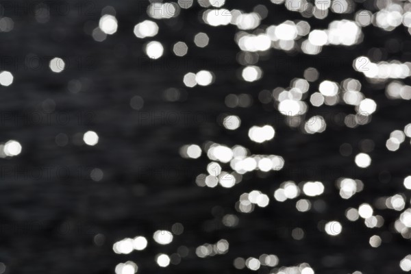 Abstract black background, sparkling white lights, bokeh balls, light reflections on water surface, octagonal light spots, copy space, background image, Sicily, southern Italy, Italy