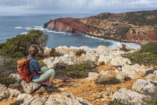 Hiking woman takes a break, view over cliff, Fishermens Trail, Rosa Vicentina, western Algarve just north of cape Cabo de Sao Vicente, Portugal