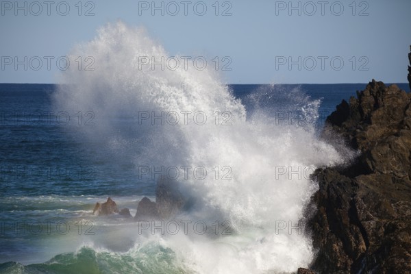 Waves crash against rocks at the mainland's easternmost point, creating rainbows in the ocean spray. Daylight, Byron Bay, New South Wales, Australia