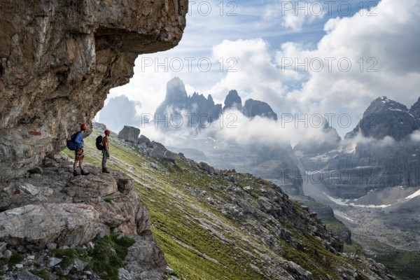 Two mountaineers on a path in front of a picturesque mountain landscape with rocky peaks, Via Ferrata SOSAT via ferrata, Cima Tosa summit in the back, Brenta Mountains, Trentino, Italy