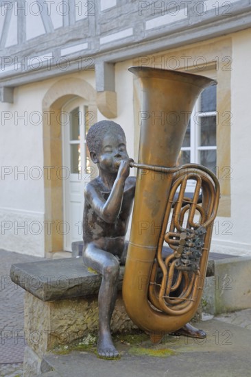 Sculpture boy with tuba by Guido Messer 1991, modern art, bronze sculpture, playing music, tuba, brass instrument, sitting, jack, size comparison, big, small, big cheeks, blowing, half-timbered house, music school, Waldenbuch, Baden-Württemberg, Germany