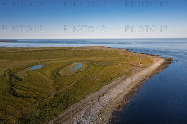 Coastal landscape on Varangerfjord with blue sky, still sea, moors and pebble beach aerial view, Barents Sea, Finnmark, Norway