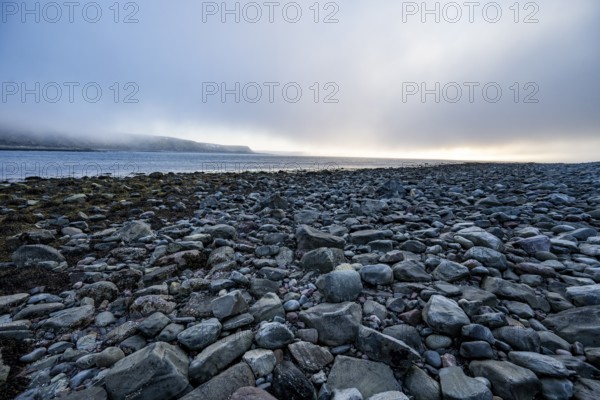 A peaceful beach at sunset with rocks and calm sea under a slightly cloudy sky, Båtsfjord, Finnmark, Norway