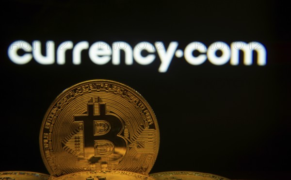 Dhaka, Bangladesh- 22 June 2025: Close-up of Bitcoin coins with the Currency.com logo visible on a screen in the background