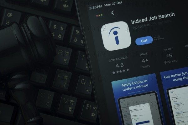 Dhaka, Bangladesh- 28 Oct 2025: An iPad displaying the Indeed app against a judge's gavel and dark keyboard background