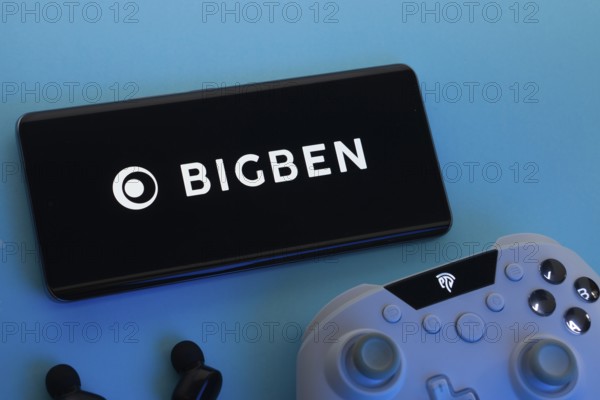 Dhaka, Bangladesh- 22 March 2025: Bigben Interactive logo displayed on a smartphone surrounded by gaming accessories in an Blue background
