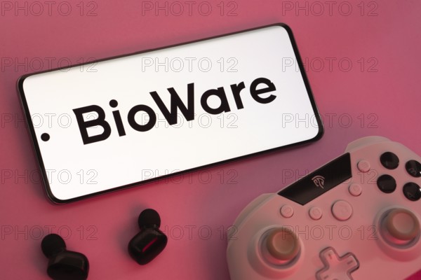 Dhaka, Bangladesh- 08 Apr 2025: A smartphone displaying the BioWare logo next to a gaming controller and earbuds on a pink surface