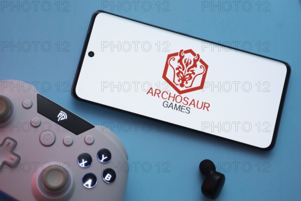 Dhaka, Bangladesh- 22 March 2025: Archosaur Games logo displayed on a smartphone surrounded by gaming accessories in an Blue background