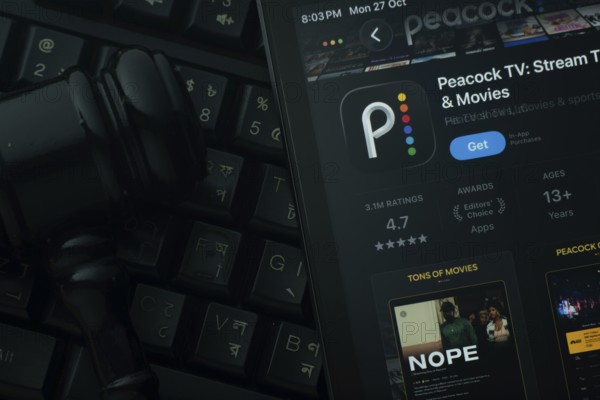 Dhaka, Bangladesh- 28 Oct 2025: An iPad displaying the Peacock TV app against a judge's gavel and dark keyboard background