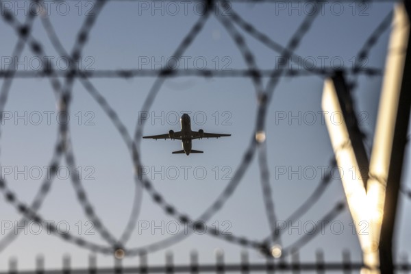 Symbolic picture security at the airport, outer fence at Düsseldorf International Airport, steel wire fence, with S-wire rollers, NATO wire, on the fence crown, airplane taking off, North Rhine-Westphalia, Germany