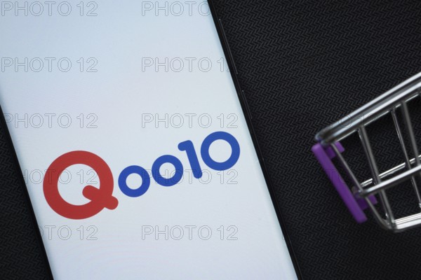 Dhaka, Bangladesh- 03 July 2025: A smartphone displaying the Qoo10 logo next to a miniature shopping cart on a background