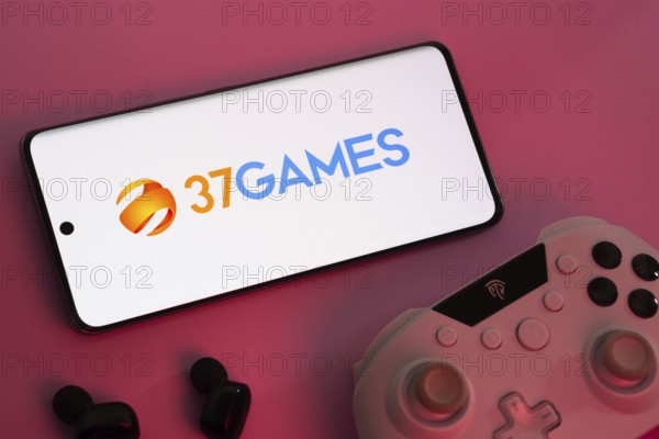 Dhaka, Bangladesh- 08 Apr 2025: A smartphone displaying the 37Games logo next to a gaming controller and earbuds on a pink surface