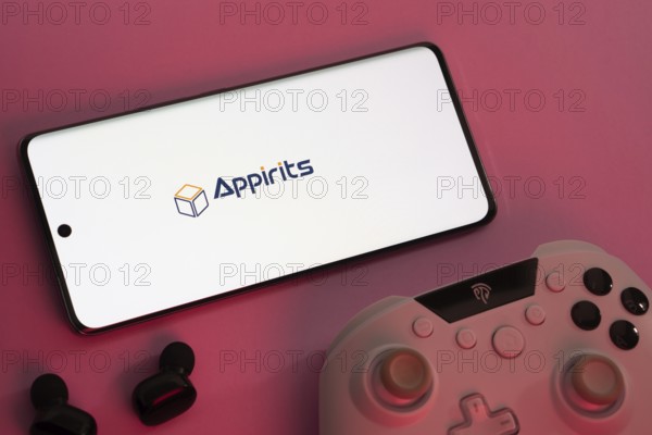 Dhaka, Bangladesh- 08 Apr 2025: A smartphone displaying the Appirits logo next to a gaming controller and earbuds on a pink surface