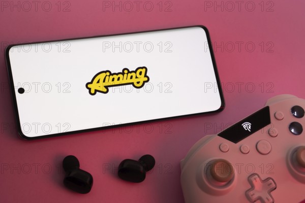 Dhaka, Bangladesh- 08 Apr 2025: A smartphone displaying the Aiming Inc logo next to a gaming controller and earbuds on a pink surface