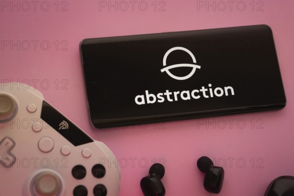 Dhaka, Bangladesh- 08 Apr 2025: A smartphone displaying the Abstraction logo next to a gaming controller and earbuds on a pink surface
