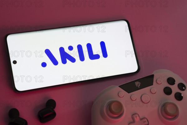 Dhaka, Bangladesh- 08 Apr 2025: A smartphone displaying the Akili Interactive logo next to a gaming controller and earbuds on a pink surface