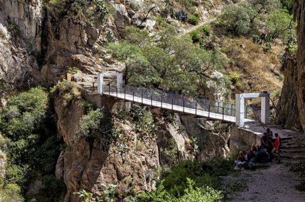 White bridge over a rocky gorge with people in shade, The landscape of the Colca Canyon in the Andes of Peru