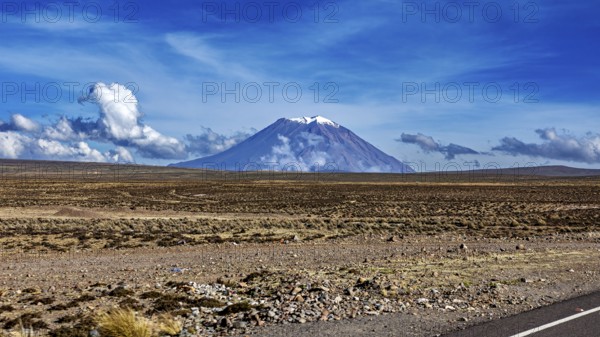 Volcano in a wide desert landscape under blue sky with clouds, snow-capped summit, The Andean highlands of Peru