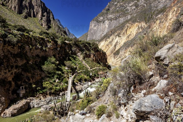 Suspension bridge spans river in deeply cut gorge with steep rocks, the landscape of Colca Canyon in the Aden of Peru