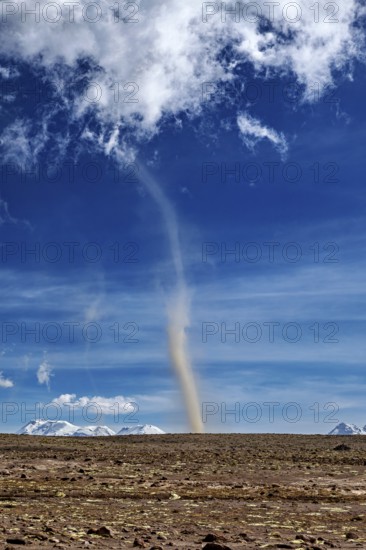 A narrow tornado crosses a dry plain, the sky is clear with scattered clouds and the mountains are visible in the background, dust devils in the Andean highlands of Peru