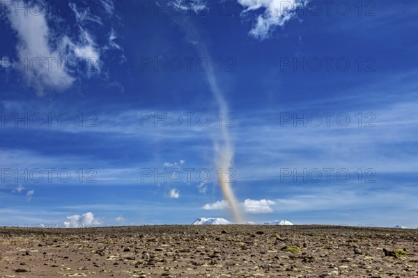 A tornado swirls dust over a dry landscape under a clear blue sky with few clouds, dust devils in the Andean highlands of Peru