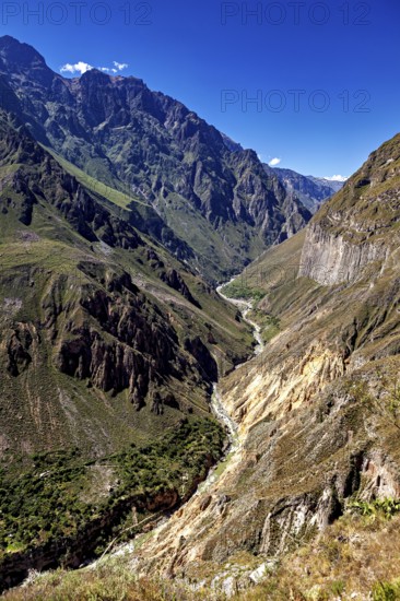 Deep gorge with a narrow river and surrounding high mountains under clear blue sky, the landscape of Colca Canyon in the Aden of Peru