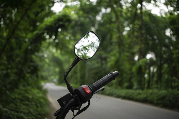 Motorcycle mirror reflecting lush green forest along a winding road, Sreepur, gazipur, Bangladesh