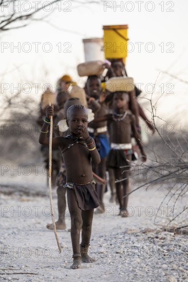 Himba woman and children run to fetch water with canisters through dry countryside, traditional Himba, Kaokoveld, Kunene, Namibia