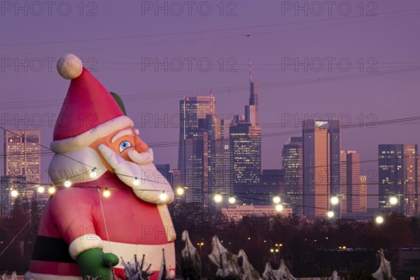 In a Christmas tree center near Frankfurt am Main, a multi-metre-high inflated figure of Santa Claus rises in front of the glowing banking skyline, Frankfurt am Main, Hesse, Germany