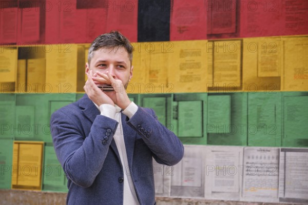 Man musician in a blue blazer and white sweater playing blues on a harmonica with eyes closed, standing outdoors in city street