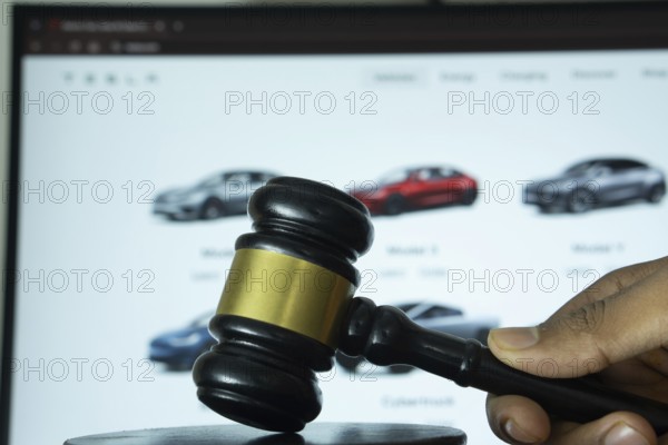 Dhaka, Bangladesh- 20 June 2025: A hand holds a gavel in front of a computer screen displaying Tesla's website