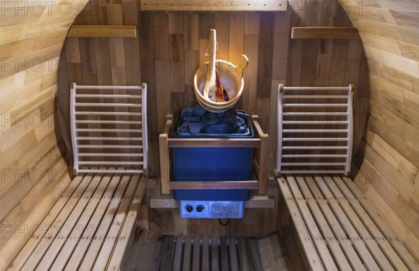 Steam and hot stone wooden cedar compact sauna interior with heating stone electrical device, hot water bucket and benches